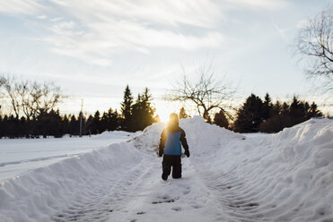 Rückansicht eines Jungen, der auf einem schneebedeckten Feld gegen den Himmel bei Sonnenuntergang läuft - CAVF59788