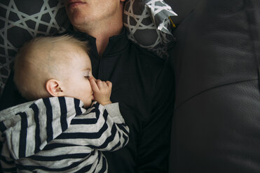 Overhead view of boy sleeping with father on sofa at home - CAVF59790