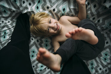 Overhead-Porträt eines fröhlichen Jungen, der zu Hause auf dem Bett spielt - CAVF59793