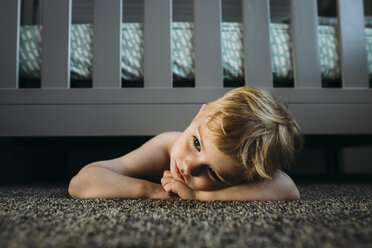 Thoughtful boy lying on rug under bed at home - CAVF59811