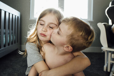 Shirtless boy kissing sister while sitting at home - CAVF59813