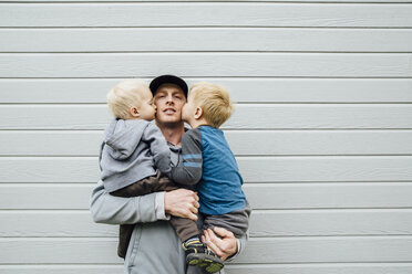 Sons kissing father while standing against wall - CAVF59828