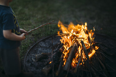 Midsection of boy holding stick while standing by fire pit - CAVF59831