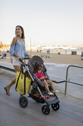 Mutter geht mit ihrer Tochter im Kinderwagen sitzend an der Strandpromenade spazieren - MAUF01899