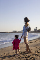 Mutter und kleine Tochter gehen am Strand spazieren und halten sich an den Händen - MAUF01902