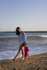 Mutter und kleine Tochter gehen am Strand spazieren und halten sich an den Händen - MAUF01903