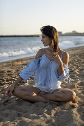 Porträt einer schönen Frau am Strand, die im Schneidersitz im Sand sitzt - MAUF01923