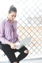 Woman sitting on chair, using laptop - ERRF00336