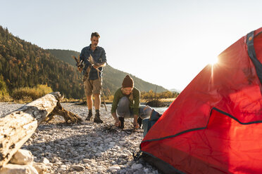 Mature couple camping at riverside, collecting wood for a camp fire - UUF16265