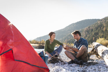 Mature couple camping at riverside in the evening light - UUF16270