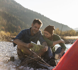 Mature couple camping at riverside, looking on map - UUF16282