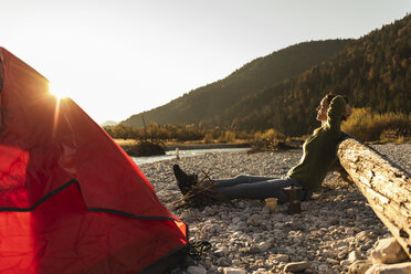 Mature woman camping at riverside in the evening light - UUF16298