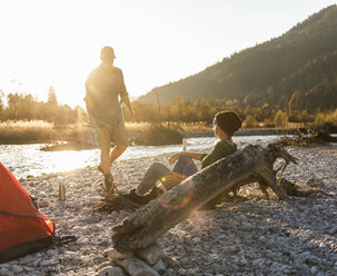 Mature couple camping at riverside, collecting wood for a camp fire - UUF16300