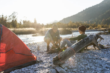 Mature couple camping at riverside, collecting wood for a camp fire - UUF16301