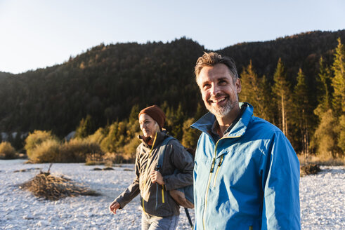 Mature couple hiking at riverside in the evening light - UUF16320