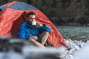 Mature man camping at riverside, drinking - UUF16327