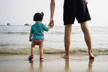 Thailand, Koh Lanta, back view of baby girl wearing UV protection shirt standing with her father at seashore - GEMF02649