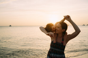 Thailand, Koh Lanta, happy mother with baby girl on her shoulders at seashore during sunset - GEMF02658