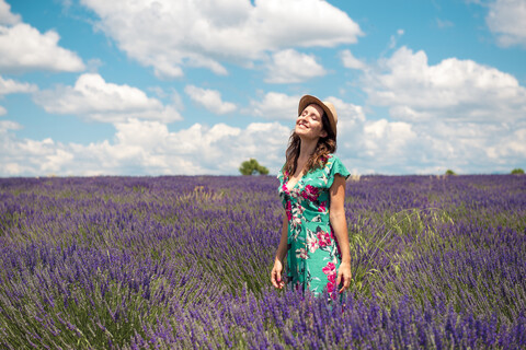 Frankreich, Provence, Valensole-Plateau, glückliche Frau mit Strohhut im Lavendelfeld stehend, lizenzfreies Stockfoto