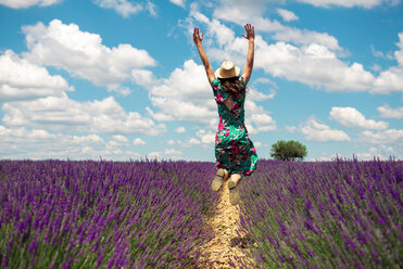 Frankreich, Provence, Hochebene von Valensole, Rückenansicht einer Frau, die zwischen Lavendelfeldern in die Luft springt, im Sommer - GEMF02666