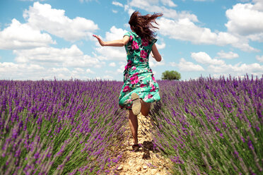 Frankreich, Provence, Hochebene von Valensole, Rückenansicht einer Frau, die im Sommer zwischen Lavendelfeldern läuft - GEMF02667