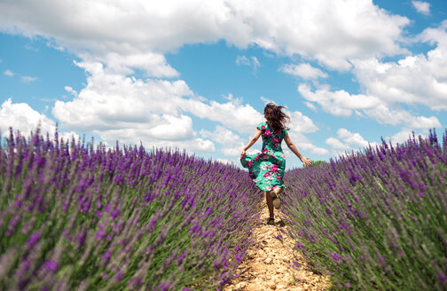 Frankreich, Provence, Hochebene von Valensole, Rückenansicht einer Frau, die im Sommer zwischen Lavendelfeldern läuft - GEMF02669