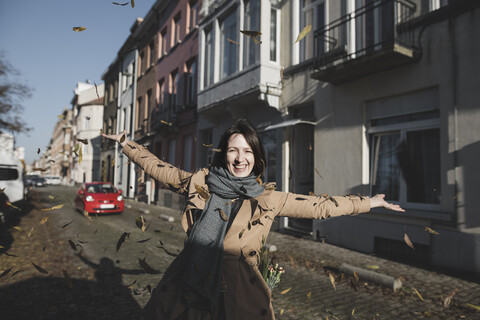 Belgien, Brüssel, Porträt einer glücklichen Frau, die Herbstblätter in die Luft wirft, lizenzfreies Stockfoto