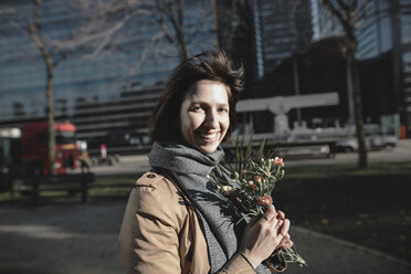 Portrait of smiling woman with bunch of flowers in the city - KMKF00678