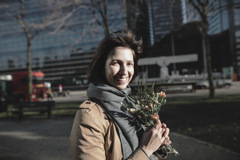Porträt einer lächelnden Frau mit Blumenstrauß in der Stadt - KMKF00678