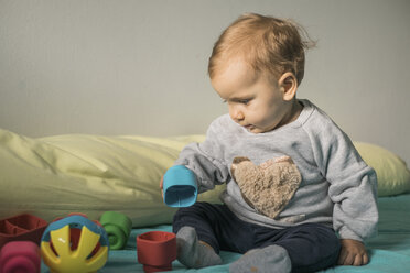 Baby Mädchen sitzt auf dem Bett und spielt mit Plastikspielzeug - MOMF00557