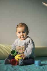 Portrait of baby girl sitting on bed playing with plastic toy - MOMF00558