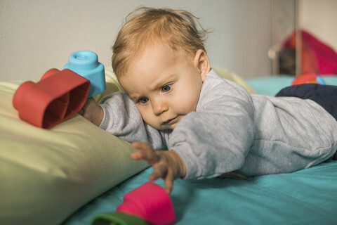 Porträt eines kleinen Mädchens, das auf dem Bett liegt und mit Plastikspielzeug spielt, lizenzfreies Stockfoto