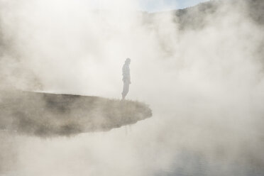 Side view of man standing by geyser amidst steam at Yellowstone National Park - CAVF59846