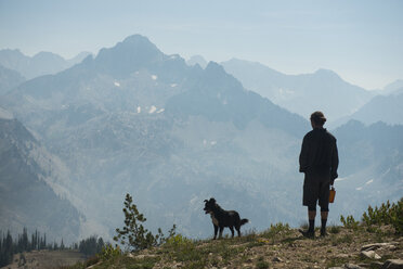 Rückansicht eines Mannes mit Hund, der auf einer Klippe in der Sawtooth Range steht - CAVF59850