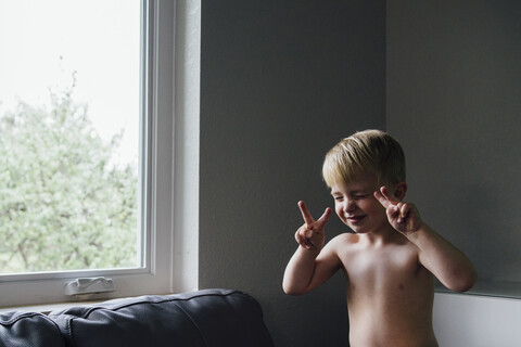 Junge gestikuliert, während er zu Hause am Fenster sitzt, lizenzfreies Stockfoto