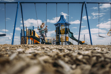 Mutter und Sohn sitzen auf einer Schaukel im Park gegen den Himmel - CAVF59896