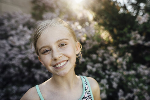 Porträt eines lächelnden Mädchens, das in einem Hinterhof vor Pflanzen steht - CAVF59899