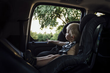 Hemdloser Babyjunge schaut durch das Fenster, während er im Autositz sitzt - CAVF59903