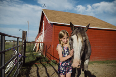 Girl stroking horse while standing at barn against sky - CAVF59906