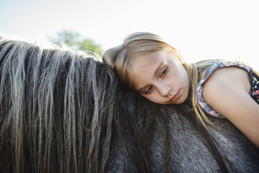 Side view of thoughtful girl lying on horse against clear sky - CAVF59910