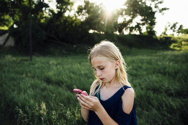 Girl using mobile phone while standing on grassy field - CAVF59914