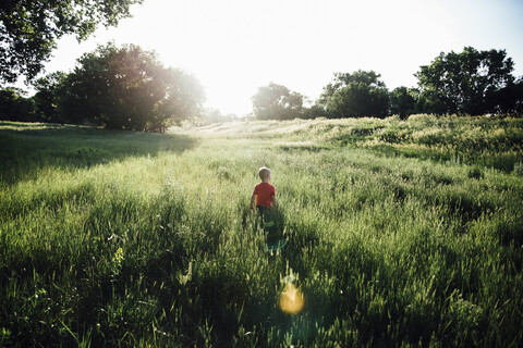 Rückansicht eines Jungen, der auf einem grasbewachsenen Feld gegen einen klaren Himmel läuft, lizenzfreies Stockfoto