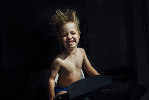 Porträt eines glücklichen Jungen ohne Hemd, der die Brise der Klimaanlage in der Dunkelkammer zu Hause genießt - CAVF59916