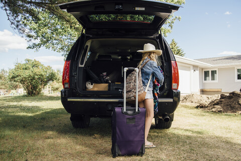 Seitenansicht eines Mädchens mit Rucksack, das am Kofferraum eines Autos steht, lizenzfreies Stockfoto