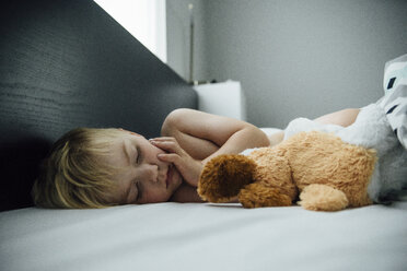 Hemdloser Junge mit Spielzeug schläft auf dem Bett zu Hause - CAVF59926