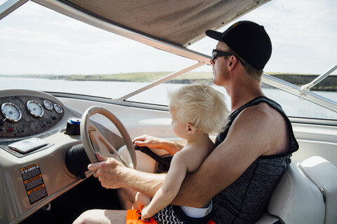 Seitenansicht eines Vaters mit seinem Sohn beim Fahren eines Motorboots, lizenzfreies Stockfoto