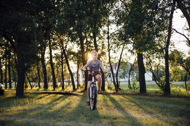Porträt eines Mädchens beim Fahrradfahren auf einer Wiese im Park - CAVF59936