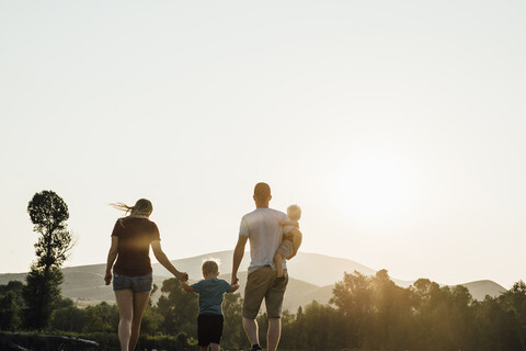 Familie spaziert auf Feld gegen klaren Himmel bei Sonnenuntergang, lizenzfreies Stockfoto