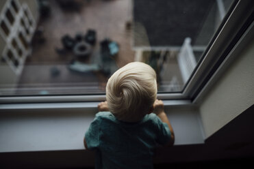 Rear view of baby boy looking through window while standing at home - CAVF59965