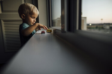 Seitenansicht eines kleinen Jungen, der mit Spielzeugautos auf der Fensterbank zu Hause spielt - CAVF59966